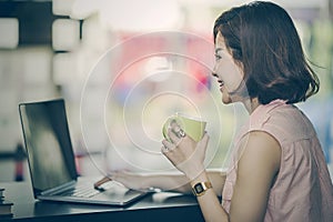 Beautiful woman holding cup of coffee and using laptop at modern