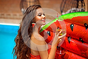 Beautiful woman Holding Glass coctail by watermelon float mattress swimming pool on villa resort. Sexy girl enjoy summer vacation