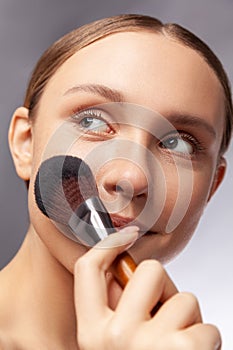 Beautiful woman holding makeup brush applying powder looking smiling away beauty visage procedures.