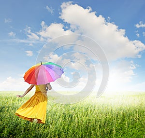 Beautiful woman holding multicolored umbrella in green grass field and cloud sky