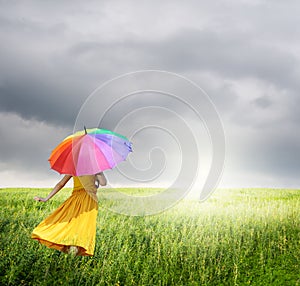 Beautiful woman holding multicolored umbrella in green grass field and raincloud