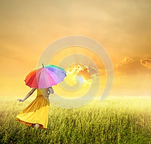 Beautiful woman holding multicolored umbrella in green grass field and sunset