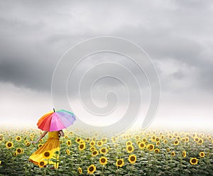 Beautiful woman holding multicolored umbrella in sunflower field and raincloud