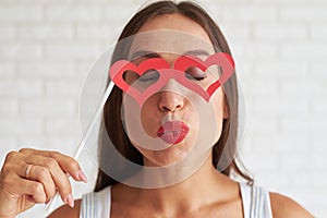 Beautiful woman holding red glasses-mask in the shape of heart a