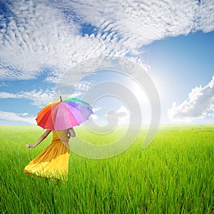 Beautiful woman holding umbrella in green grass field and bule sky