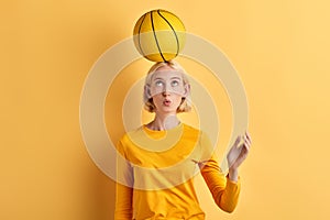 Beautiful woman holds basket ball on head isolated on yellow background