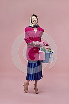 A beautiful woman holds a bucket of cleaning tools in her hands. Bright makeup.