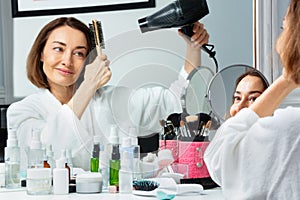 Beautiful woman in housecoat holding hairdryer dry hair