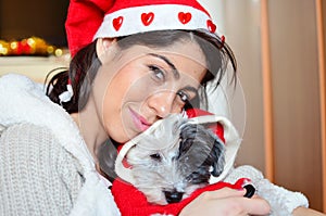 Beautiful woman hugging her dog with red christmas hat