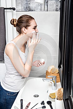 Beautiful woman hydrating her face in bathroom with makeup accessories