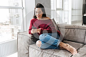 Beautiful woman indoors in home on sofa using mobile phone