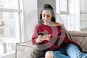 Beautiful woman indoors in home on sofa using mobile phone