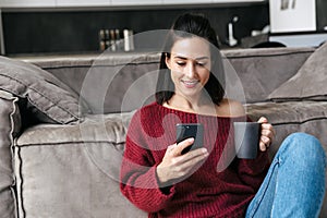 Beautiful woman indoors in home using mobile phone drinking coffee