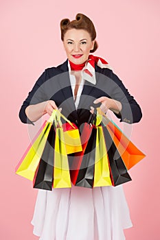 Beautiful woman in jacket with colored shopping paper bags over rose pink background. Charming beautiful brunette shopping time