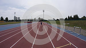 A beautiful woman jogger starts running at the city athletics stadium during a day training in slow motion 4K video on