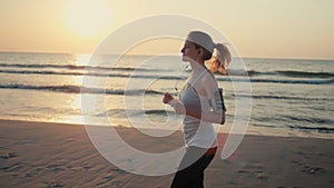 Beautiful Woman is Jogging on Sea Coast at Sunset, Running on Beach with Phone