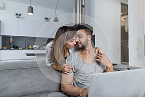 Beautiful Woman Kiss Man Sitting On Couch With Laptop Computer In Modern Apartment Young Couple Spend Time Together At