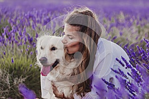 Beautiful woman kissing her golden retriever dog in lavender fields at sunset. Pets outdoors and lifestyle