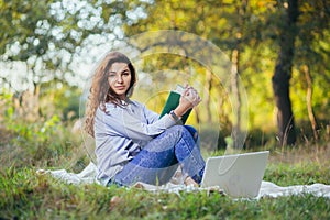 Beautiful woman with laptop and book on the grass