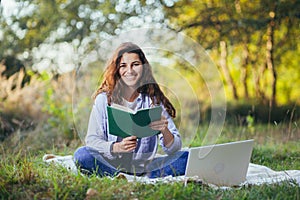 Beautiful woman with laptop and book on the grass