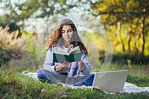 Beautiful woman with laptop and book on the grass