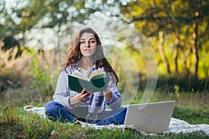 Beautiful woman with laptop and book on the grass