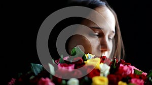 Beautiful woman with a large bouquet of flowers in her arms smelling a fragrant colorful roses on black background