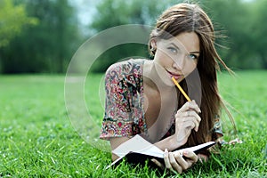 Beautiful woman lays on a grass in park with a diary in ha