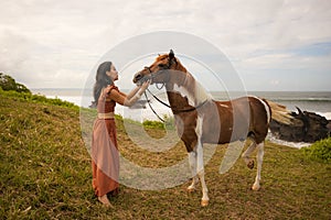 Beautiful woman leading horse by its reins. Horse riding. Human and animals relationship. Nature concept. Bali