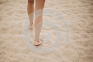 Beautiful woman legs barefoot walking on sandy beach, carefree vacation mood. Stylish young female relaxing on coast, cropped view