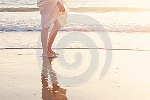 Beautiful woman legs on the beach with sea surf at sunset. Romanc step on surf