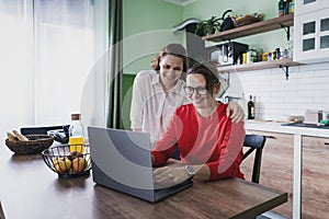 Beautiful woman lesbian couple talking and using laptop and smartphone at kitchen room, couple living together at home