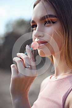 Beautiful woman licking a lollipop close-up. Red shadows on the eyes of a girl, professional makeup, natural cosmetics