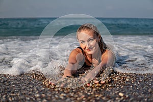 A beautiful woman lies on the shore of the ocean and listens to the smooth surf of the waves, enjoys a summer day, in the