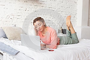 a beautiful woman lies on a white bed with a gray laptop next to