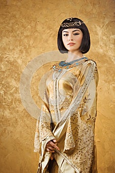 Beautiful woman like Egyptian Queen Cleopatra on golden background