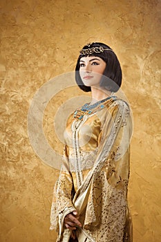 Beautiful woman like Egyptian Queen Cleopatra on golden background