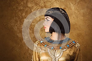 Beautiful woman like Egyptian Queen Cleopatra on golden background. Side view, face profile