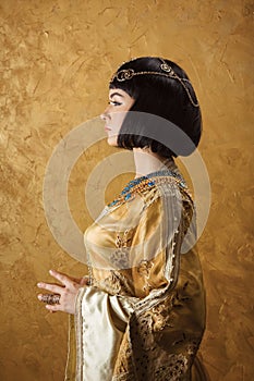 Beautiful woman like Egyptian Queen Cleopatra on golden background. Side view, face profile