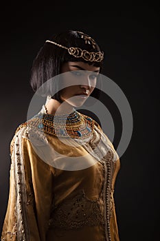 Beautiful woman like Egyptian Queen Cleopatra with serius face on black background.