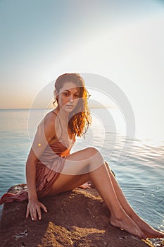 Beautiful woman in lingerie posing on a coastal cliff. Sea and sunset in the background. Vertical orientation