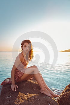 Beautiful woman in lingerie posing on a coastal cliff. Sea and sunset in the background. Vertical orientation. Wild look