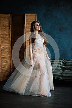 Beautiful woman in lingerie showing long legs sexy pose standing at bed over her bedroom near big window. Bride boudoir. Wedding