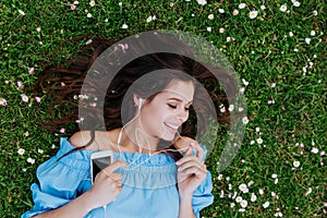 Beautiful woman listening to music with headphones and lying in a garden of flowers