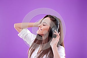 Beautiful woman listening to music using wireless headphones in studio isolated over purple background.