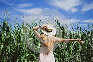 Beautiful woman with long blond hair in hat walking in cornfield