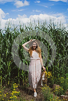 Beautiful woman with long blond hair in hat walking in cornfield