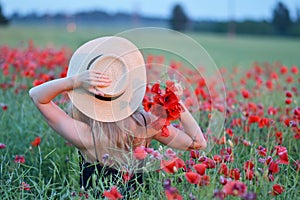 Beautiful woman with long blond hair in hat walking in the field with poppies