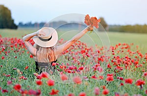 Beautiful woman with long blond hair in hat walking in the field with poppies