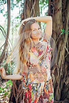 Beautiful woman with long blond hair poses on the background of trees. Portrait of a young long-haired girl